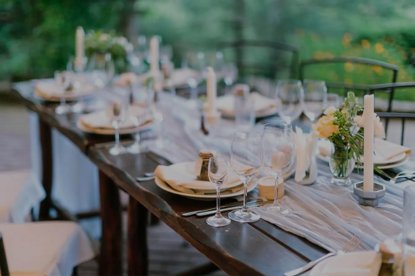 Long wooden table set for an outdoor dinner with candles and flowers