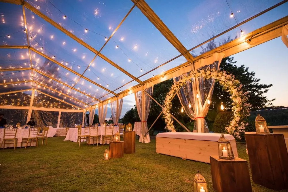 Clear tent with string lights and a floral arch at dusk
